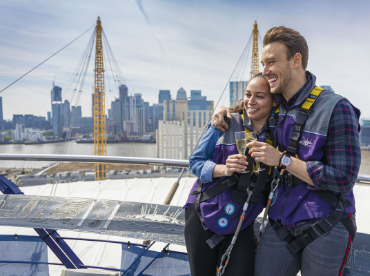 A young couple enjoy a glass of champagne from the roof of The O2 after their climb to the summit.